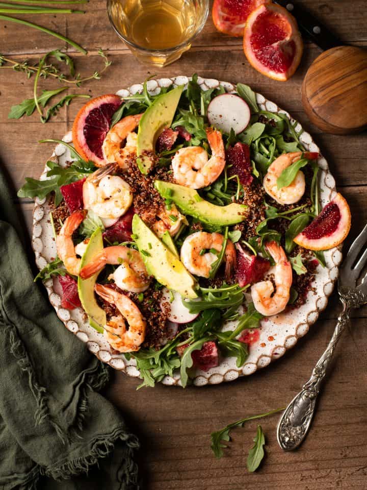 A plate of salad with arugula, blood orange slices, avocado slices and shrimp.